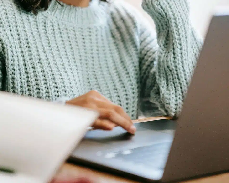 Frau in hellblauem Pullover sitzt am Laptop und nimmt an einem Online Kreativ Workshop teil